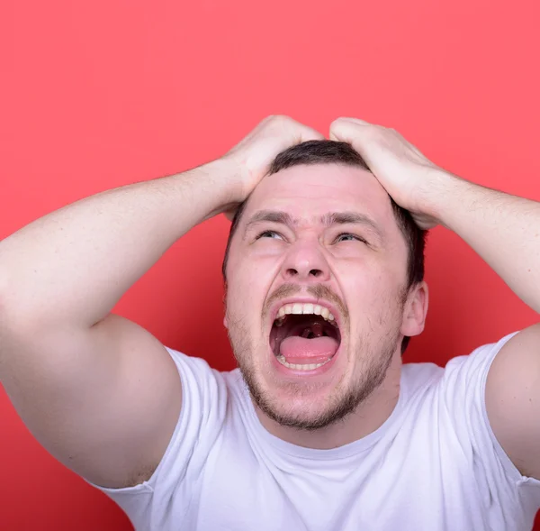 Portrait of angry man screaming and pulling hair against red bac — Stock Photo, Image