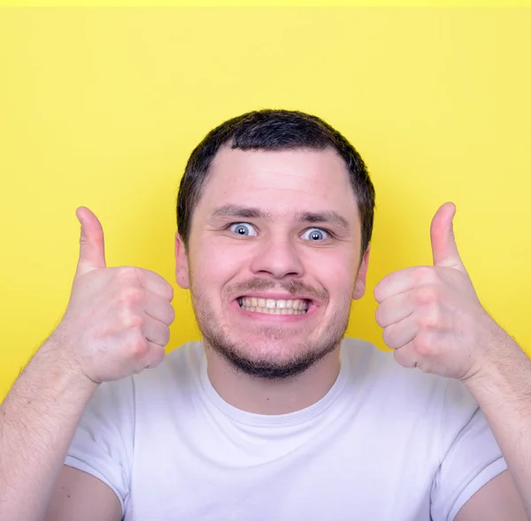 Portrait of with funny expression holding thumbs up against yell — Stock Photo, Image