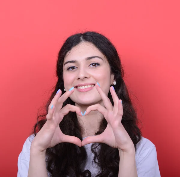 Portrait of happy woman making heart shape with hands against re — Stock Photo, Image