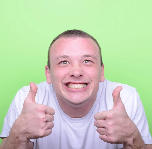 Portrait of with funny expression holding thumbs up against gree — Stock Photo, Image