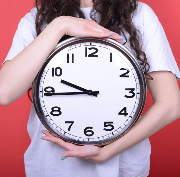 Portrait of girl holding huge office clock against red backgroun — Stock Photo, Image