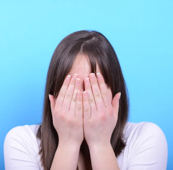 Portrait of covering her face with hands against blue background — Stock Photo, Image