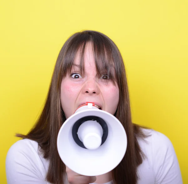 Portrait of young woman shouting with a megaphone against yellow — Stock Photo, Image