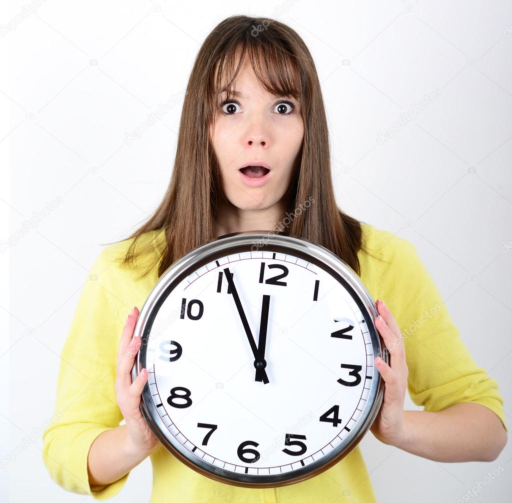 Portrait of a young female holding big clock against white backg