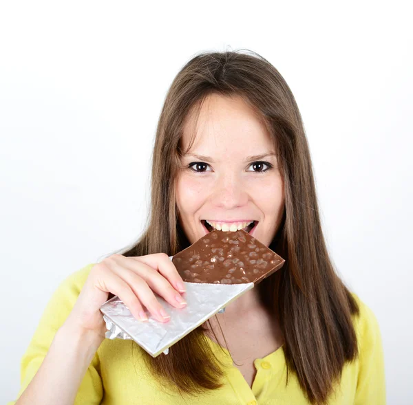 Jovem mulher comendo barra de chocolate contra fundo branco — Fotografia de Stock