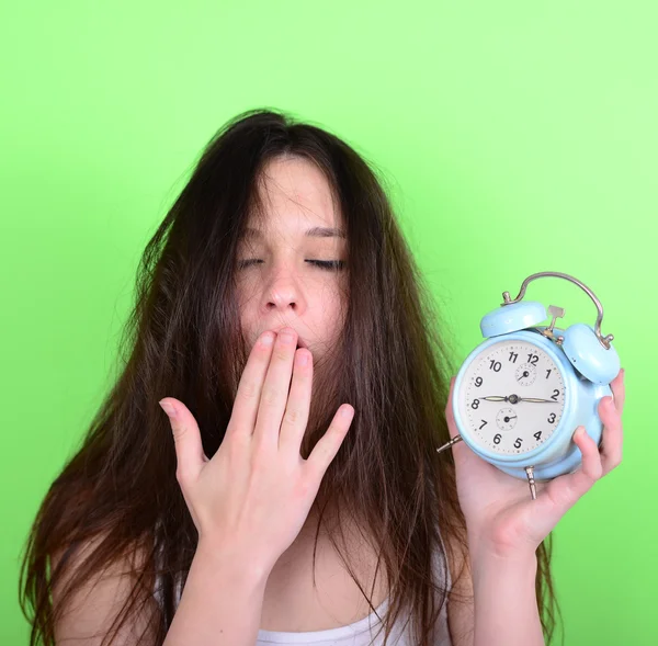 Portrait of sleepy young female in chaos holding clock against g — Stock Photo, Image
