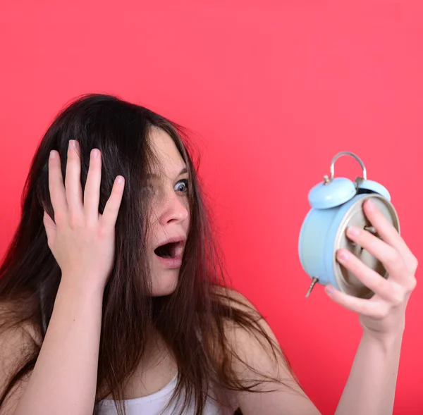Portrait of sleepy young female in chaos holding clock against r — Stock Photo, Image