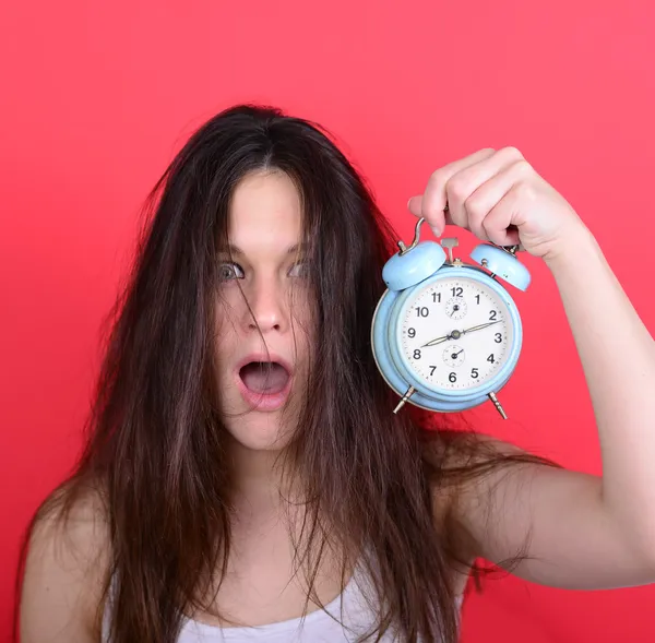 Portrait of sleepy young female in chaos holding clock against r — Stock Photo, Image