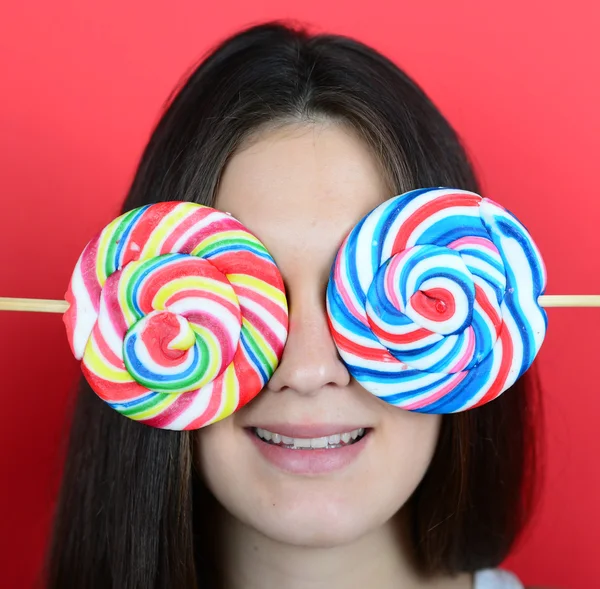Portrait of woman covering eyes with lollipops against red backg — Stock Photo, Image