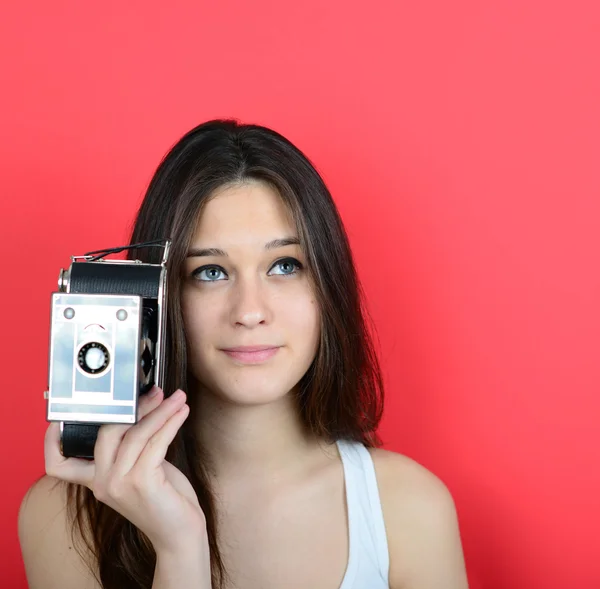 Retrato de una joven hembra sosteniendo una cámara vintage contra una espalda roja — Foto de Stock