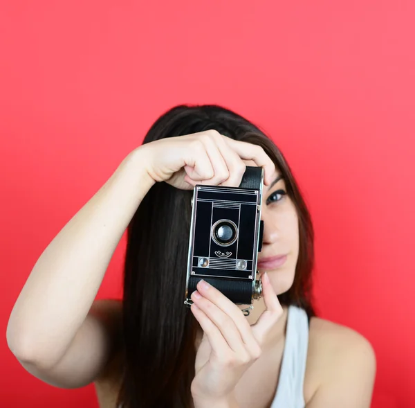 Retrato de jovem fêmea segurando câmera vintage contra costas vermelhas — Fotografia de Stock