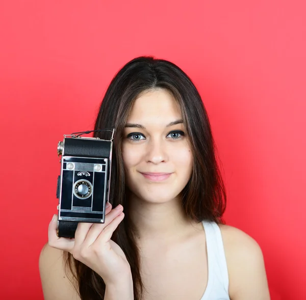 Portrait of young female holding vintage camera against red back — Stock Photo, Image