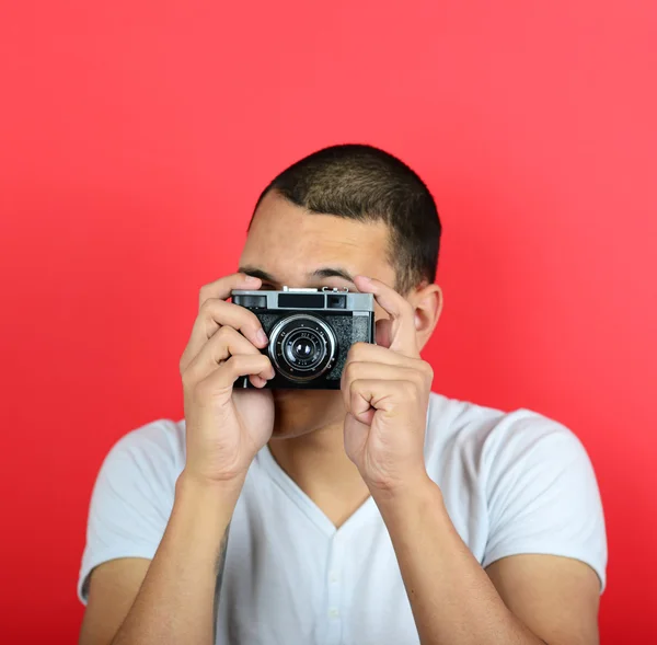 Portrait of young male holding vintage camera against red backgr — Stock Photo, Image