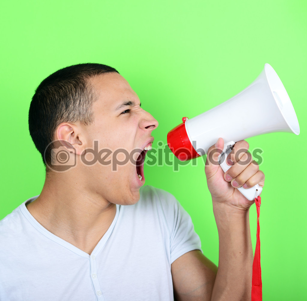 Portrait of young man shouting with a megaphone against green ba