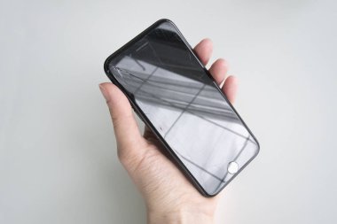 Broken iPhone in a womans hand on a light background. Black smartphone with cracks on the screen