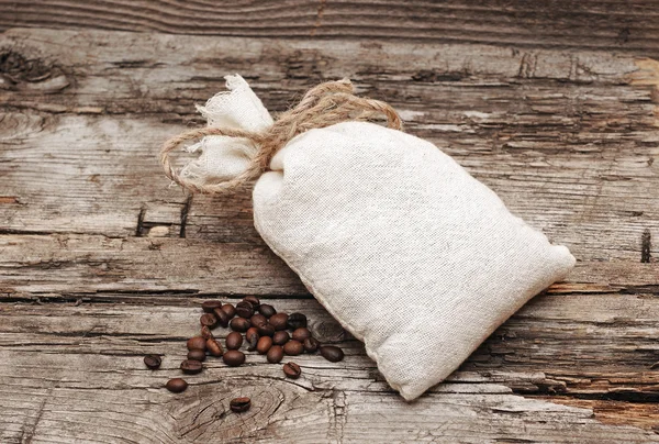 Koffiebonen en jute zak op houten achtergrond — Stockfoto