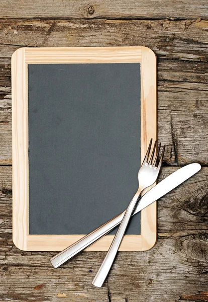 Menu blackboard lying on wooden table with knife and fork — Stock Photo, Image