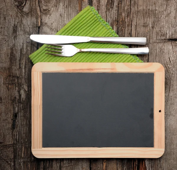 Menu blackboard lying on old wooden table with knife and fork — Stock Photo, Image