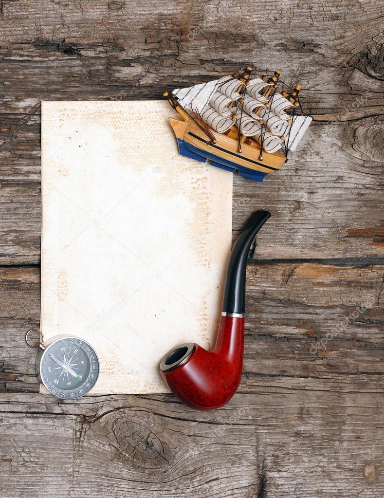 pipe, old paper, compass and model classic boat on wood backgrou