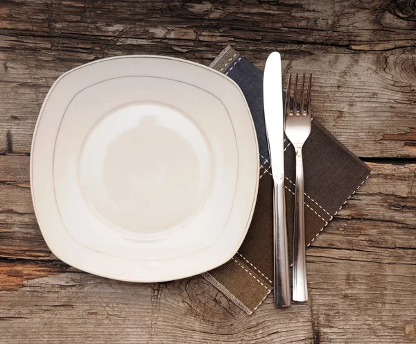 Empty dish, knife and fork and brown napkin on old wood table — Stock Photo, Image