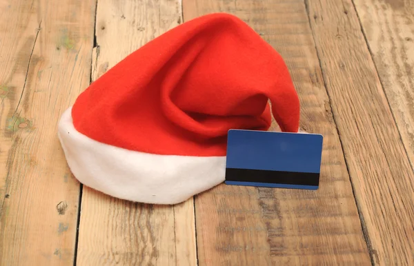 Sombrero de Santa Claus con tarjeta de crédito en blanco sobre fondo de madera —  Fotos de Stock