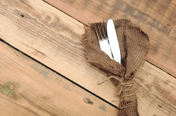 Knife and fork in rough old sacking over wood — Stock Photo, Image