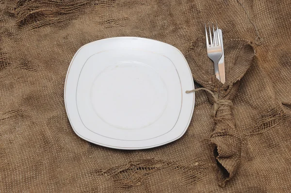 Empty white plate fork and knife on brown sacking texture — Stock Photo, Image