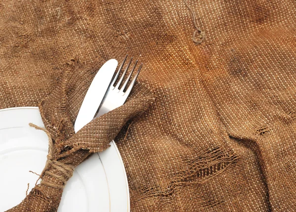 Eine Platteneinfassung mit silberner Gabel und Messer auf alter Säckeltextur — Stockfoto