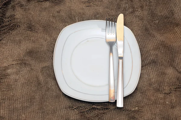 Empty white plate fork and knife on brown sacking texture — Stock Photo, Image