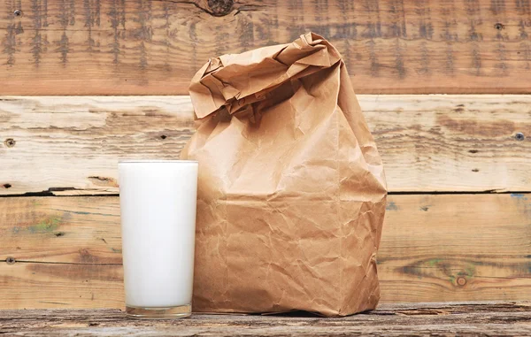 木製の背景上のガラスのミルクと紙弁当袋 — ストック写真