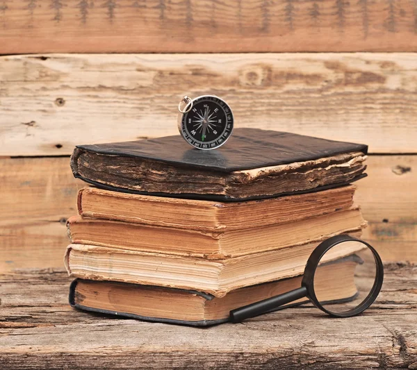 Pila di libri antichi con bussola e lente d'ingrandimento su woo — Foto Stock