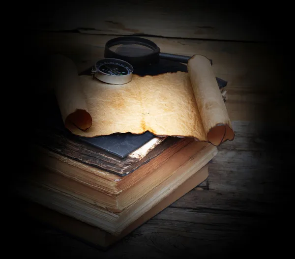 Stack of antique books with compass, magnifying glass and paper — Stock Photo, Image