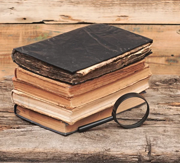 Pilha de livros antigos com lupa na mesa de madeira — Fotografia de Stock