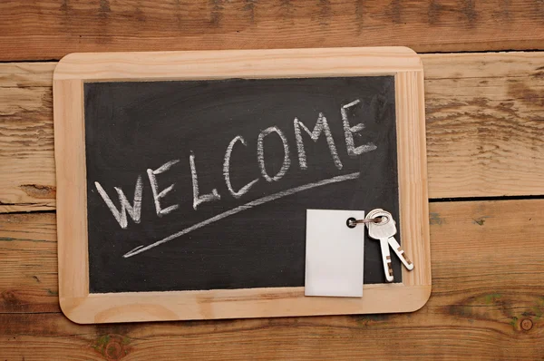 Palabra "bienvenida" y la llave en la pequeña escuela pizarra de madera —  Fotos de Stock