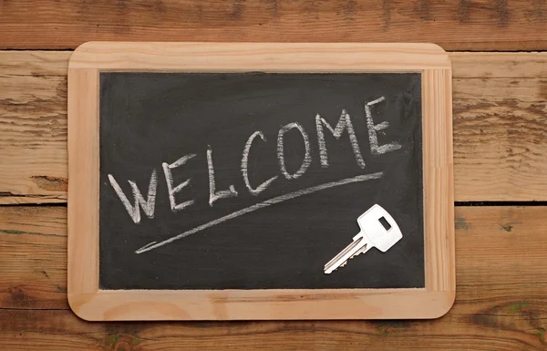 Palabra "bienvenida" y la llave en la pequeña escuela pizarra de madera —  Fotos de Stock