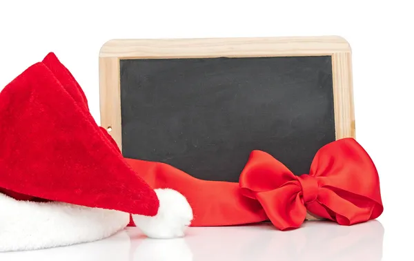 Beyaz zemin üzerine kırmızı kabarık Noel Baba şapkası ile küçük yazı tahtası — Stok fotoğraf