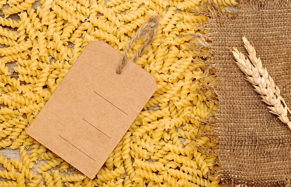 Pasta cruda, prezzo e spighe di grano con etichetta come sfondo — Foto Stock