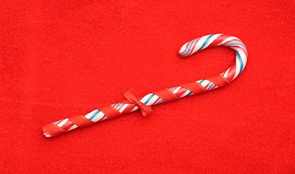 Un bastón de caramelo con un lazo sobre un fondo de textura roja —  Fotos de Stock