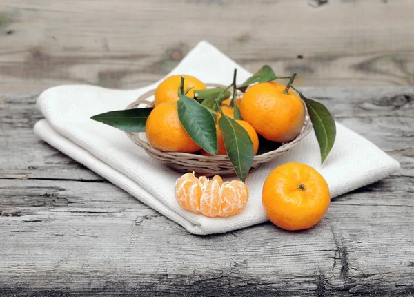 Mandarinen mit Blättern in einem schönen Korb auf einem Holztisch — Stockfoto