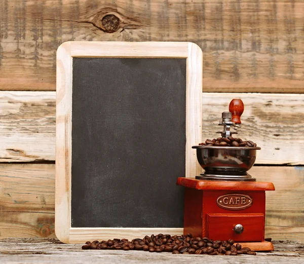 Coffee mill and blank chalkboard over wooden background — Stock Photo, Image