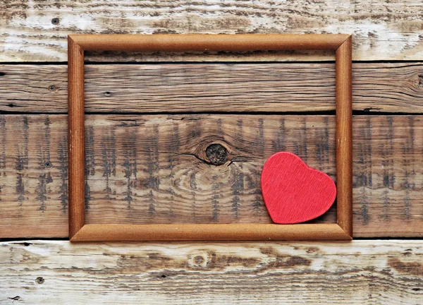 Um coração vermelho em uma moldura de madeira velha em uma parede áspera velha . — Fotografia de Stock