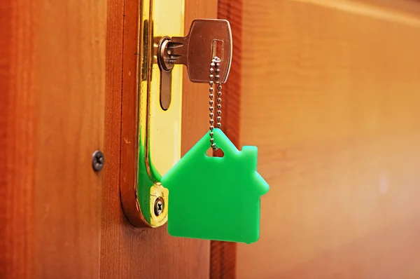 Llave de la casa en un llavero en forma de casa en la cerradura de una puerta — Foto de Stock