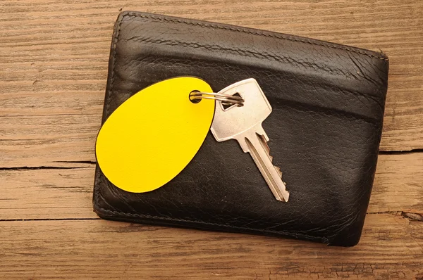 Wallet and key with blank label on wood background — Stock Photo, Image