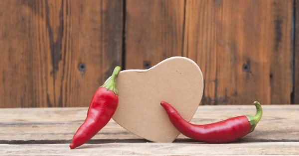 Rote Chilischoten mit Herz aus Pappe auf Holzhintergrund — Stockfoto