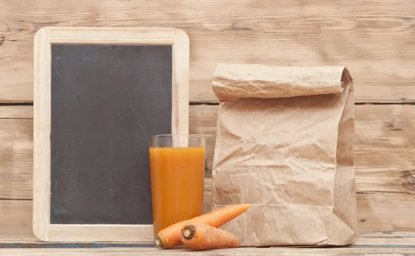 Cibo sano - carote e succo di carote con sacchetto di carta su legno — Foto Stock