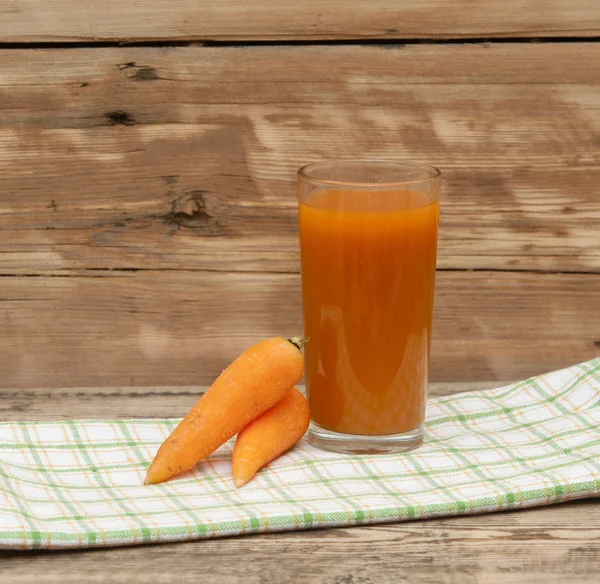 Verre de jus de carotte et de carottes mûres sur une serviette colorée — Photo
