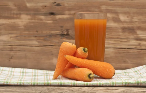 Glass of carrot juice and ripe carrots on colorful napkin — Stock Photo, Image