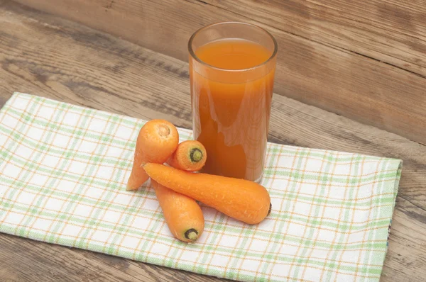 Verre de jus de carotte et de carottes mûres sur une serviette colorée — Photo