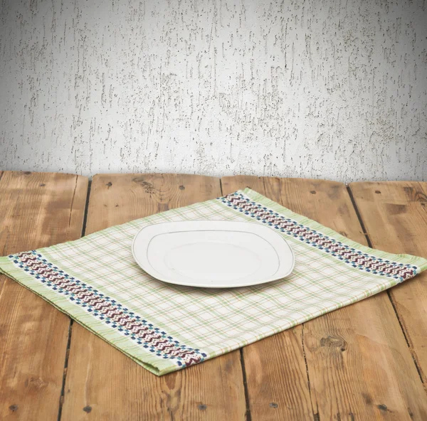 Empty plate on tablecloth on wooden table over grunge background — Stock Photo, Image