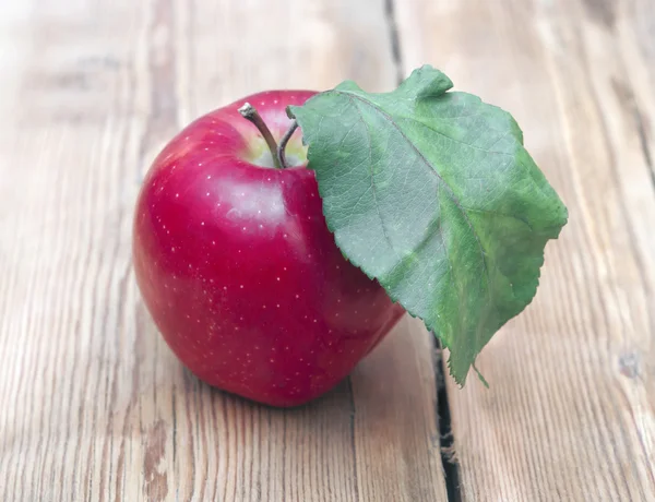 Rött äpple med gröna blad på trä bakgrund — Stockfoto
